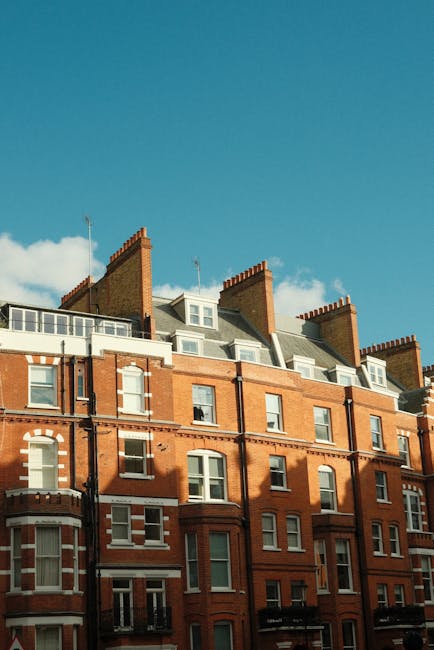 The image depicts the upper floors of a historic red-brick residential building with white window frames and decorative architectural details under a bright blue sky with scattered clouds. The buildin